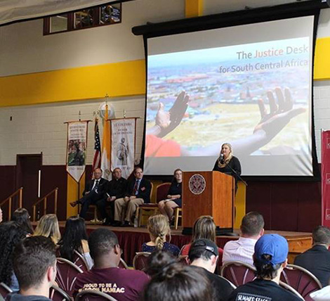 Jessica Dewhurst speaks to the Iona College campus community during her keynote speech. Seated on stage (l-r) are Dr. Joseph  Nyre, Iona College President, Br. Kevin Griffith, ERCBNA Province Leader, Carl Procario-Foley, Ph.D, Director of Iona College Mission and Ministry, and Iona College SGA President Hannah McGowan.
